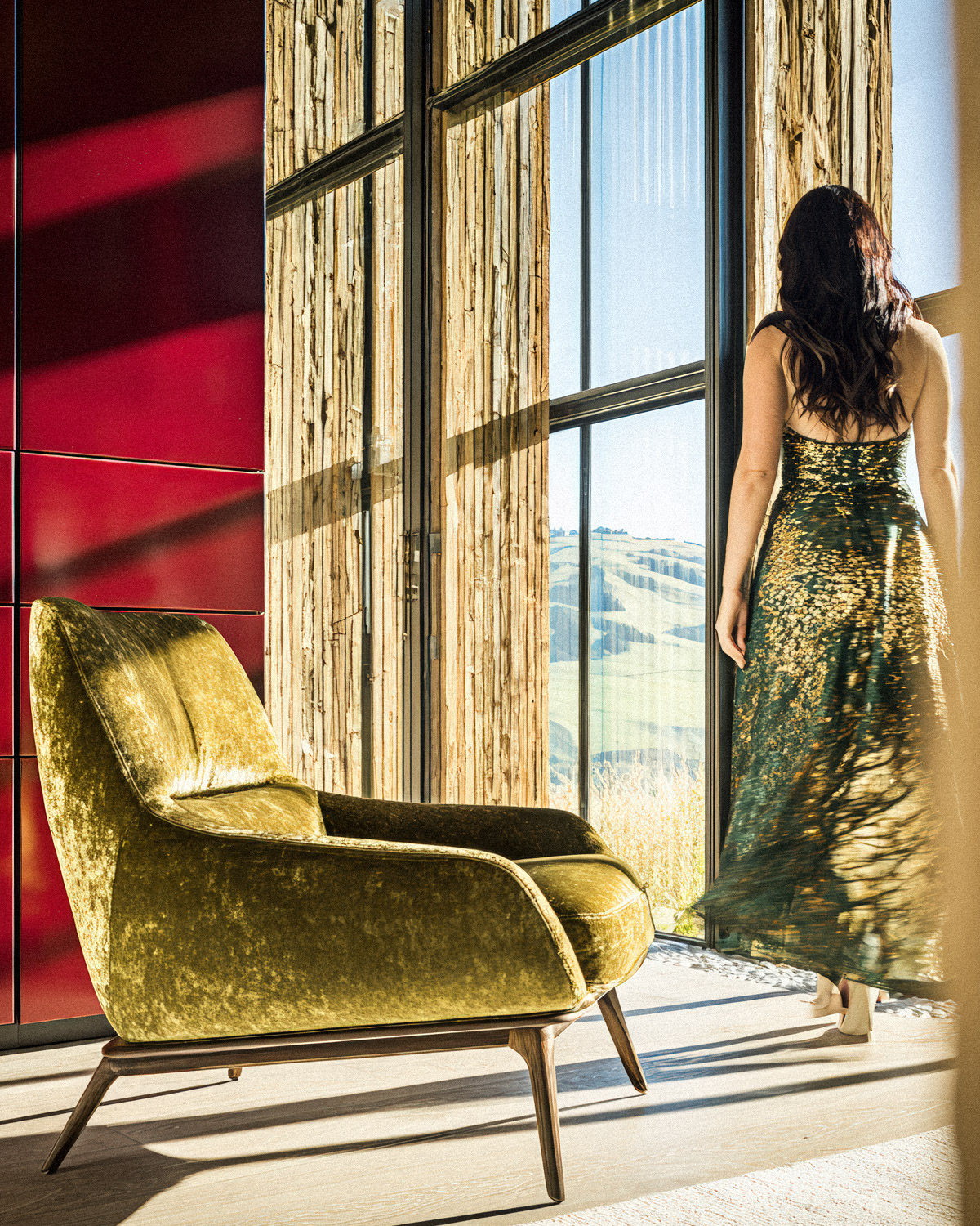 femme-contemplation-mur-rouge-cardinal-tendance-2026 Femme contemplant le paysage près fauteuil velours avec mur rouge cardinal en arrière-plan