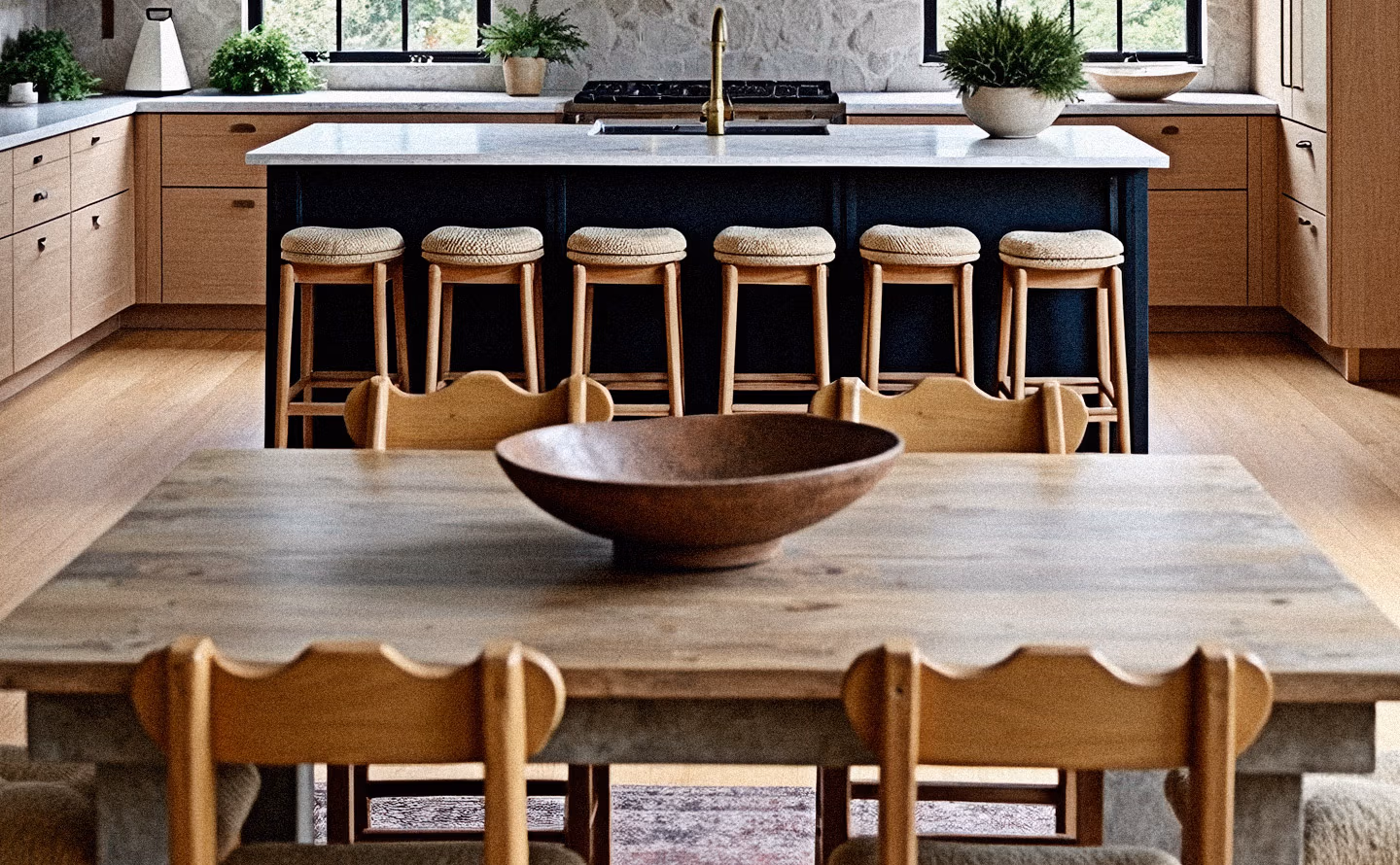 Cuisine contemporaine sophistiquée avec îlot central noir et plans de travail pierre claire, meubles en bois naturel, six tabourets bouclette beige et au premier plan grande table en bois massif brut avec chaises scandinaves illustrant l'intégration harmonieuse de pièces patrimoniales dans décor moderne Cuisine contemporaine sophistiquée avec îlot central noir et plans de travail pierre claire, meubles en bois naturel, six tabourets bouclette beige et au premier plan grande table en bois massif brut avec chaises scandinaves illustrant l'intégration harmonieuse de pièces patrimoniales dans décor moderne