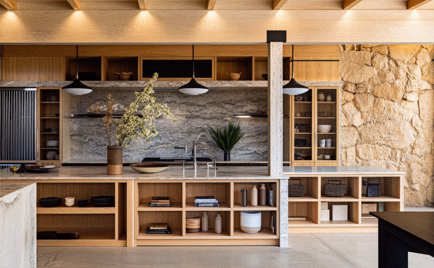Cuisine contemporaine rangements ouverts bois naturel façon bibliothèque, mur pierre apparente, plafond poutres bois, suspensions noires, plan travail marbre gris, continuité visuelle matériaux Cuisine contemporaine rangements ouverts bois naturel façon bibliothèque, mur pierre apparente, plafond poutres bois, suspensions noires, plan travail marbre gris, continuité visuelle matériaux