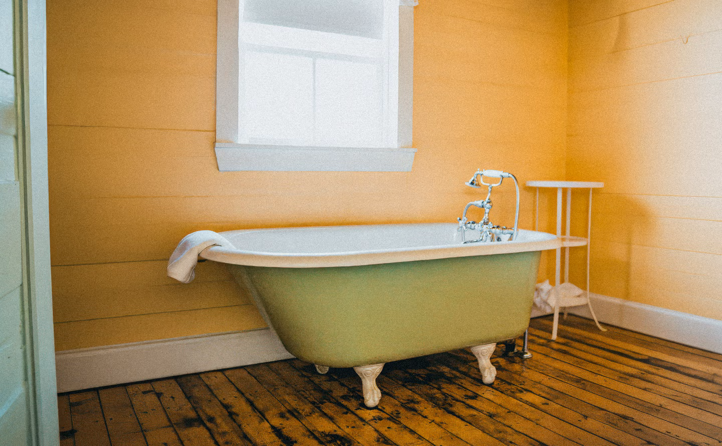 Baignoire sur pieds vintage vert sauge, murs lambris bois jaune moutarde, sol parquet bois ancien patiné, robinetterie chromée rétro, salle de bain invités palette cohérente Baignoire sur pieds vintage vert sauge, murs lambris bois jaune moutarde, sol parquet bois ancien patiné, robinetterie chromée rétro, salle de bain invités palette cohérente