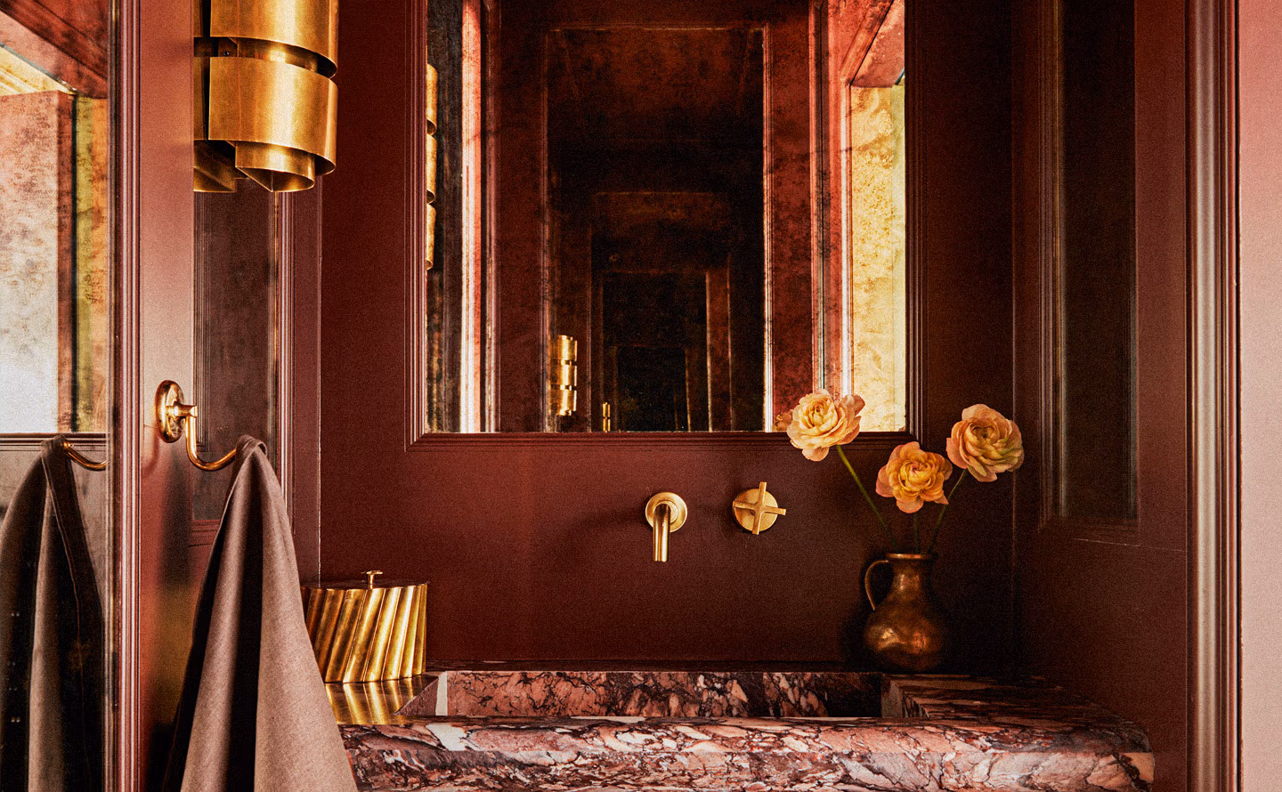 Toilettes invités luxueuses aux murs bordeaux profond avec panneaux muraux encadrant miroir central, plan vasque en marbre rose rouge veiné spectaculaire, robinetterie murale laiton doré brossé, lustre circulaire art déco doré suspendu, appliques murales laiton, vase cuivré ancien contenant roses orange pêche, serviettes taupe suspendues à patères dorées illustrant comment interventions architecturales sophistiquées (panneaux, moulures, matériaux nobles) transforment espace fonctionnel exigu en micro-architecture mémorable théâtrale. Toilettes invités luxueuses aux murs bordeaux profond avec panneaux muraux encadrant miroir central, plan vasque en marbre rose rouge veiné spectaculaire, robinetterie murale laiton doré brossé, lustre circulaire art déco doré suspendu, appliques murales laiton, vase cuivré ancien contenant roses orange pêche, serviettes taupe suspendues à patères dorées illustrant comment interventions architecturales sophistiquées (panneaux, moulures, matériaux nobles) transforment espace fonctionnel exigu en micro-architecture mémorable théâtrale.