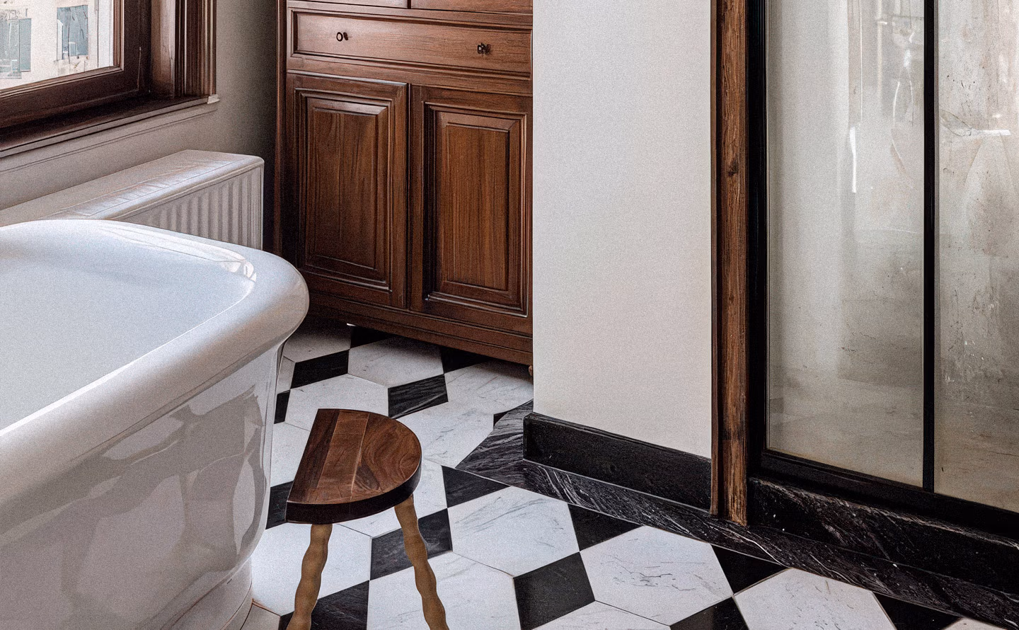 Salle de bain au caractère narratif avec carrelage damier noir et blanc inspiré d'une église, meuble ancien en bois sombre, baignoire blanche classique et miroir patiné illustrant l'ancrage de souvenirs personnels dans la matière décorative Salle de bain au caractère narratif avec carrelage damier noir et blanc inspiré d'une église, meuble ancien en bois sombre, baignoire blanche classique et miroir patiné illustrant l'ancrage de souvenirs personnels dans la matière décorative