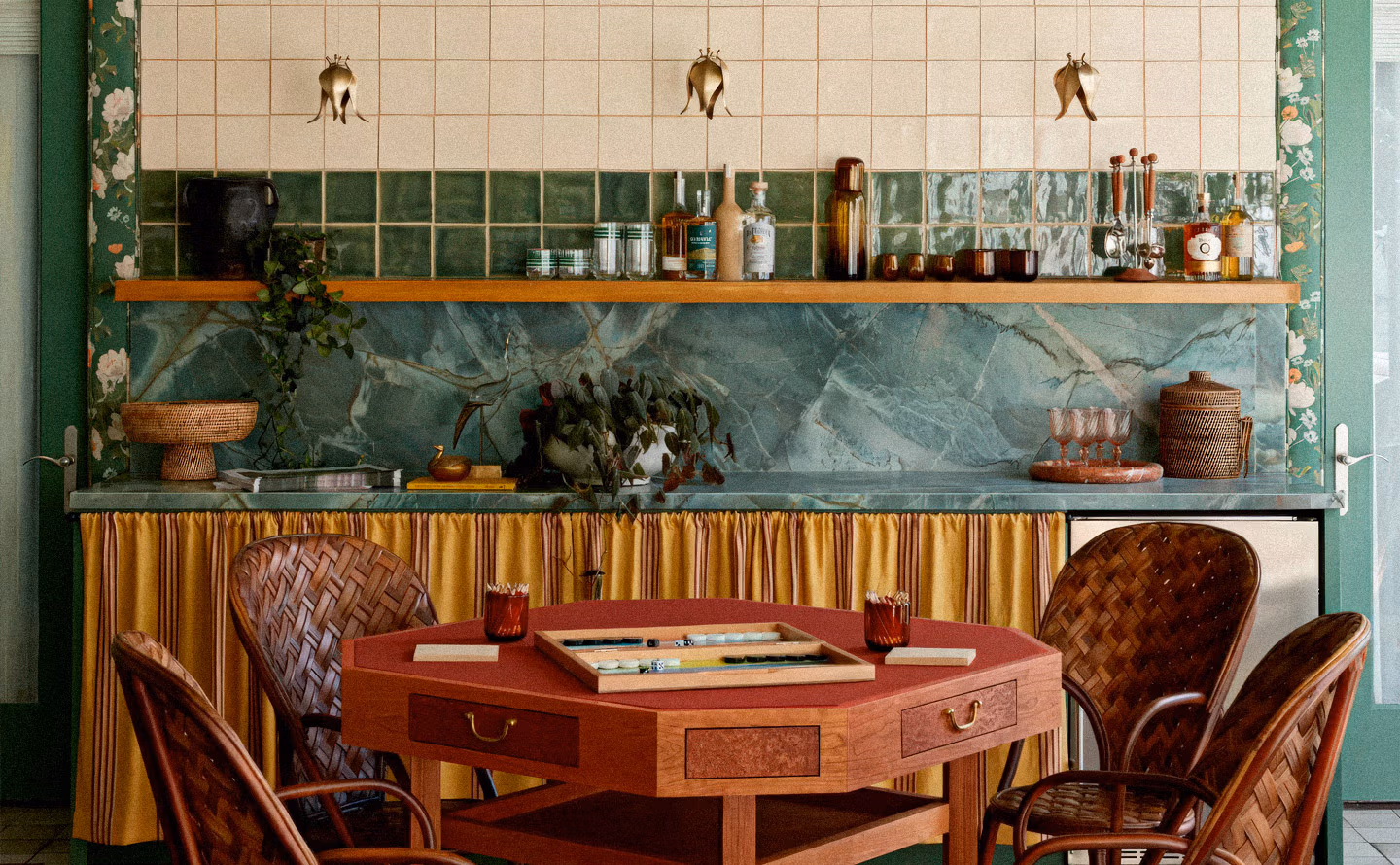 Cuisine bar maximiste avec papier peint floral vert émeraude, carrelage beige et bande émaillée verte, crédence marbre vert veiné spectaculaire, étagère bois chargée de spiritueux et verrerie, appliques laiton tulipes, rideau plissé jaune moutarde sous plan de travail et table de jeu centrale rouge avec chaises rotin tressé illustrant l'adoucissement textile dans décor saturé Cuisine bar maximiste avec papier peint floral vert émeraude, carrelage beige et bande émaillée verte, crédence marbre vert veiné spectaculaire, étagère bois chargée de spiritueux et verrerie, appliques laiton tulipes, rideau plissé jaune moutarde sous plan de travail et table de jeu centrale rouge avec chaises rotin tressé illustrant l'adoucissement textile dans décor saturé