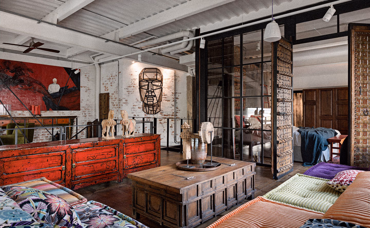 Loft industriel aux murs de briques blanches patinées avec commode ancienne orange vermillon craquelée surmontée de sculptures de chevaux en bois brut, grande verrière d'atelier noire, îlot central en bois ancien à plateau extensible, chapiteau corinthien détourné en support de bougies et vases, lustre cage géométrique métal, créant un espace où les antiquités s'intègrent fonctionnellement au quotidien. Loft industriel aux murs de briques blanches patinées avec commode ancienne orange vermillon craquelée surmontée de sculptures de chevaux en bois brut, grande verrière d'atelier noire, îlot central en bois ancien à plateau extensible, chapiteau corinthien détourné en support de bougies et vases, lustre cage géométrique métal, créant un espace où les antiquités s'intègrent fonctionnellement au quotidien.