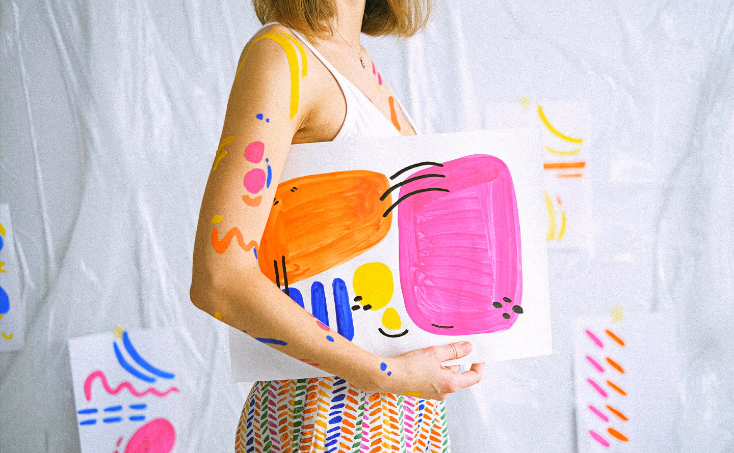 Femme présentant toile abstraite peinte à la main aux formes organiques colorées rose fuchsia, orange vif, jaune citron et bleu cobalt, devant rideau blanc également décoré de motifs peints spontanés, illustrant la création artistique personnelle DIY pour galerie murale domestique singulière et l'émancipation des codes académiques de l'art mural. Femme présentant toile abstraite peinte à la main aux formes organiques colorées rose fuchsia, orange vif, jaune citron et bleu cobalt, devant rideau blanc également décoré de motifs peints spontanés, illustrant la création artistique personnelle DIY pour galerie murale domestique singulière et l'émancipation des codes académiques de l'art mural.