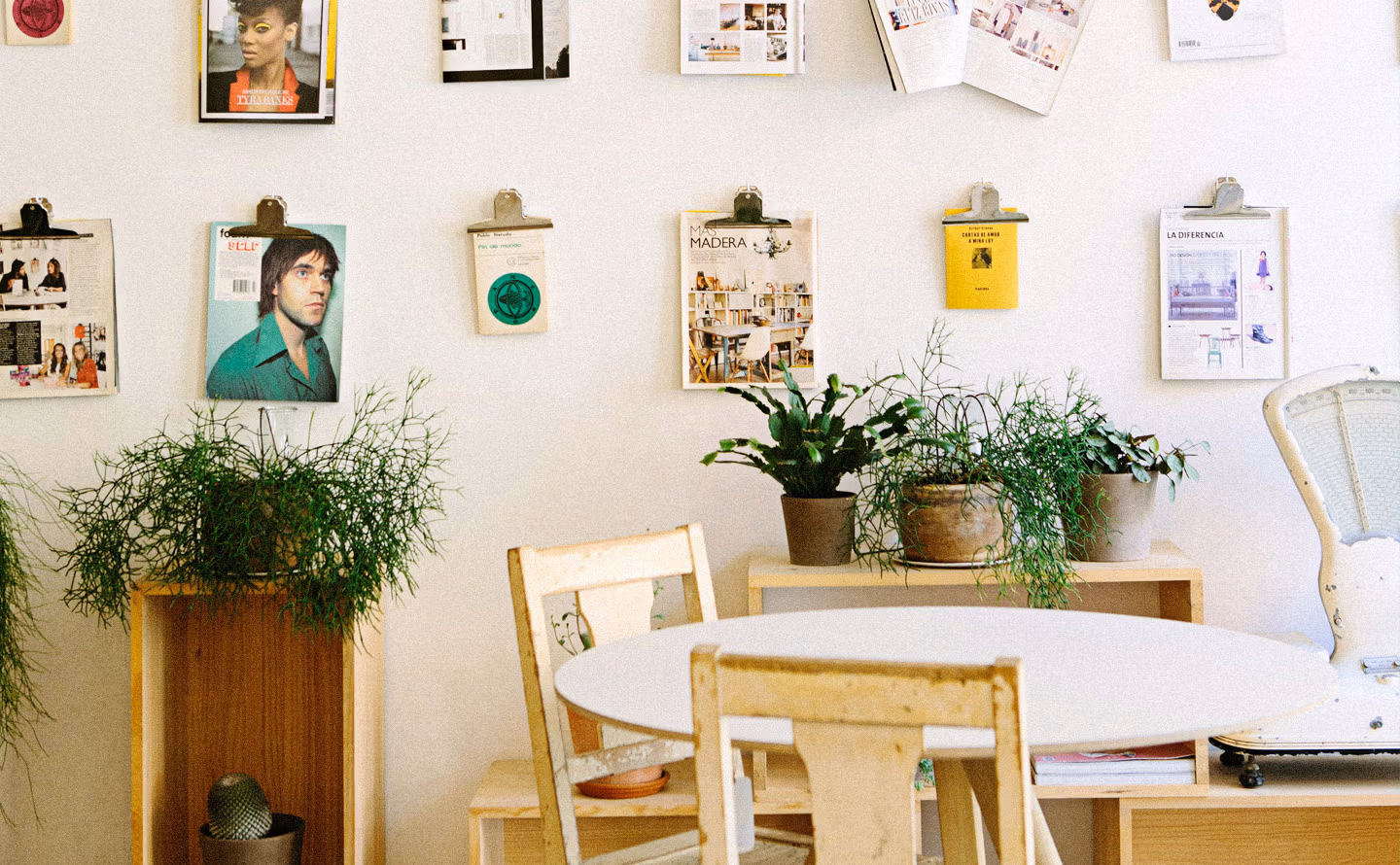 Espace de travail créatif lumineux avec mur inspiration composé de planches à pince dorées vintage présentant photos magazines, planches tendances et images colorées, table ronde blanche entourée de chaises en bois clair dépareillées, plantes vertes luxuriantes débordantes dans pots terre cuite et cache-pots chinés variés, illustrant la stratification organique d'éléments récupérés plutôt que l'achat coordonné neuf. Espace de travail créatif lumineux avec mur inspiration composé de planches à pince dorées vintage présentant photos magazines, planches tendances et images colorées, table ronde blanche entourée de chaises en bois clair dépareillées, plantes vertes luxuriantes débordantes dans pots terre cuite et cache-pots chinés variés, illustrant la stratification organique d'éléments récupérés plutôt que l'achat coordonné neuf.