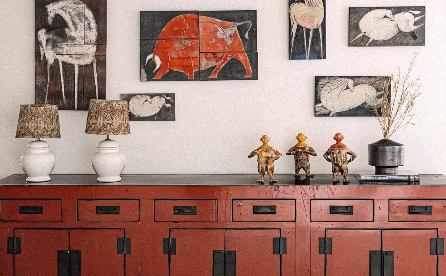 Console chinoise ancienne rouge bordeaux patinée à multiples tiroirs et portes avec ferrures noires, collection murale d'estampes animalières encadrées (taureau rouge central, chevaux blancs stylisés), paire de lampes pied porcelaine blanche avec abat-jour décorés motifs bruns, trois figurines patinées dorées rouge, vase noir graphite contenant branches séchées, illustrant la philosophie d'investissement décoratif privilégiant acquisition de pièces de qualité intemporelles qui s'apprécient avec le temps plutôt que multiplication d'achats éphémères standardisés. Console chinoise ancienne rouge bordeaux patinée à multiples tiroirs et portes avec ferrures noires, collection murale d'estampes animalières encadrées (taureau rouge central, chevaux blancs stylisés), paire de lampes pied porcelaine blanche avec abat-jour décorés motifs bruns, trois figurines patinées dorées rouge, vase noir graphite contenant branches séchées, illustrant la philosophie d'investissement décoratif privilégiant acquisition de pièces de qualité intemporelles qui s'apprécient avec le temps plutôt que multiplication d'achats éphémères standardisés.