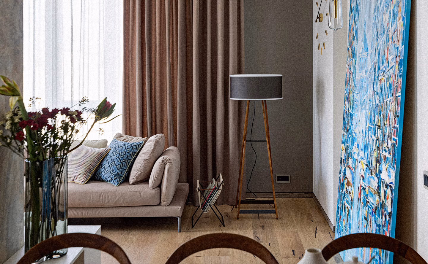 Salon contemporain avec grand tableau abstrait bleu en grand format sur mur kaki, canapé beige avec coussins graphiques, lampadaire tripode bois à abat-jour anthracite, rideaux taupe et bouquet de fleurs fraîches illustrant la philosophie du vivre avec ses pièces d'art et design au quotidien plutôt que de les sanctuariser. Salon contemporain avec grand tableau abstrait bleu en grand format sur mur kaki, canapé beige avec coussins graphiques, lampadaire tripode bois à abat-jour anthracite, rideaux taupe et bouquet de fleurs fraîches illustrant la philosophie du vivre avec ses pièces d'art et design au quotidien plutôt que de les sanctuariser.