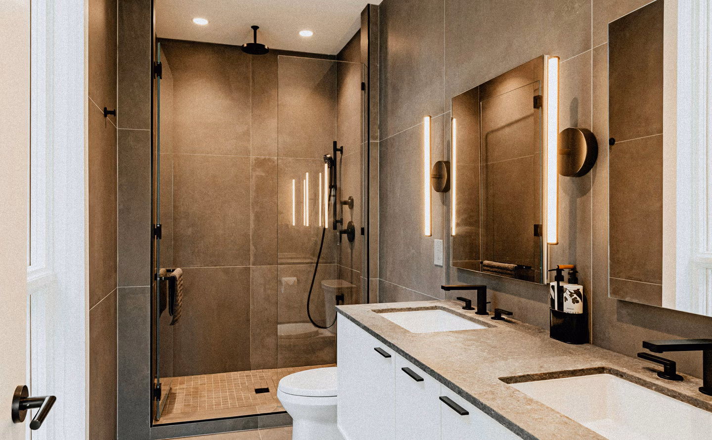 Salle de bains contemporaine épurée avec carrelage grand format beige taupe, double vasque encastrée blanche dans meuble laqué blanc à poignées noires, robinetterie noire mate, miroir lumineux LED vertical, douche à l'italienne avec paroi vitrée noire illustrant qu'investir dans cet espace intime du quotidien avec matériaux nobles et finitions soignées transforme la routine en rituel luxueux quotidien. Salle de bains contemporaine épurée avec carrelage grand format beige taupe, double vasque encastrée blanche dans meuble laqué blanc à poignées noires, robinetterie noire mate, miroir lumineux LED vertical, douche à l'italienne avec paroi vitrée noire illustrant qu'investir dans cet espace intime du quotidien avec matériaux nobles et finitions soignées transforme la routine en rituel luxueux quotidien.