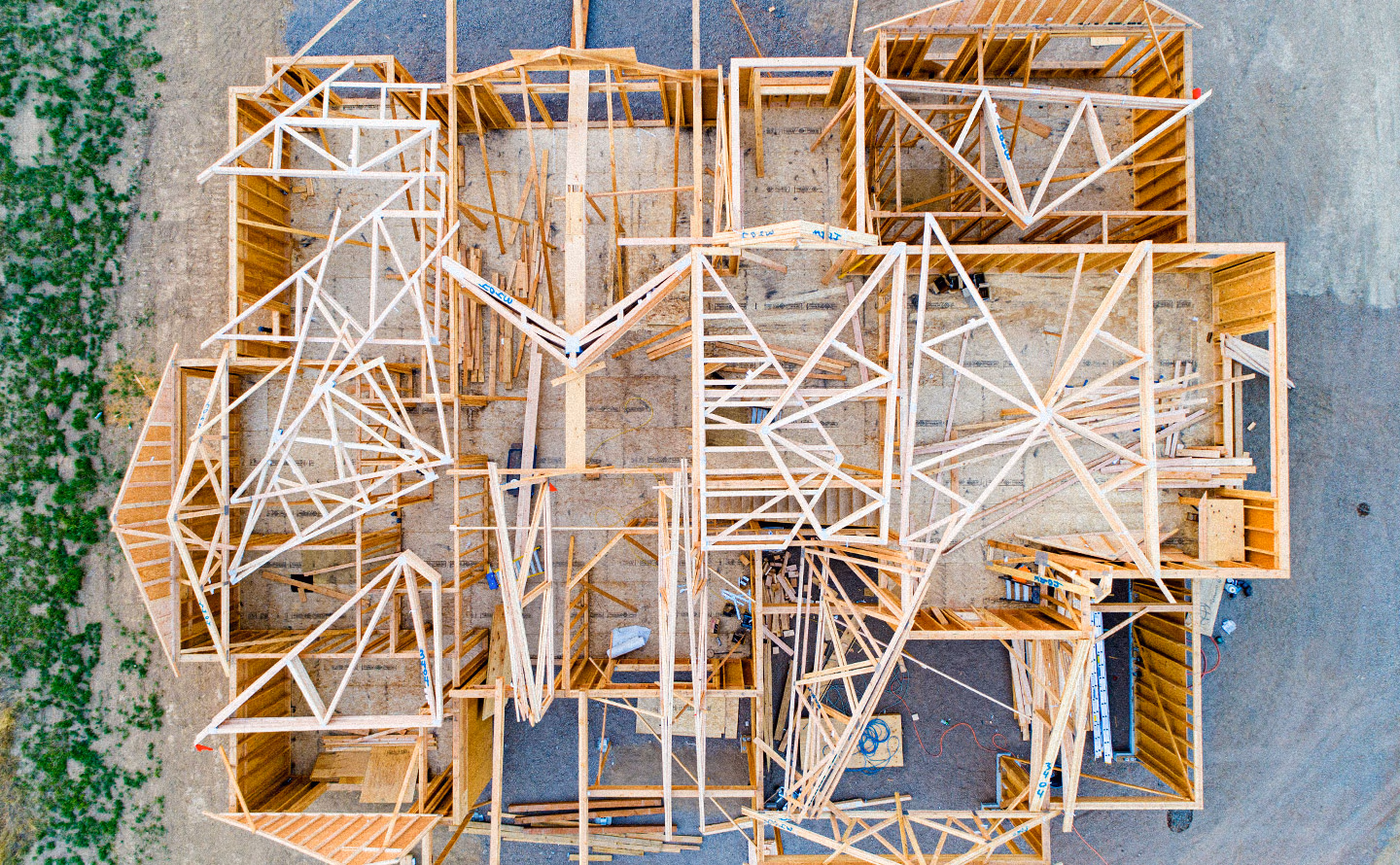 Vue aérienne drone d'une maison en construction montrant la complexité structurelle avec charpentes en bois brut, fermes triangulées, cloisons multiples, fondations béton et échafaudages illustrant de manière humoristique qu'un plan d'agencement rigoureux constitue la partition invisible fondamentale déterminant toute la cohérence spatiale future avant même de penser au mobilier esthétique. Vue aérienne drone d'une maison en construction montrant la complexité structurelle avec charpentes en bois brut, fermes triangulées, cloisons multiples, fondations béton et échafaudages illustrant de manière humoristique qu'un plan d'agencement rigoureux constitue la partition invisible fondamentale déterminant toute la cohérence spatiale future avant même de penser au mobilier esthétique.