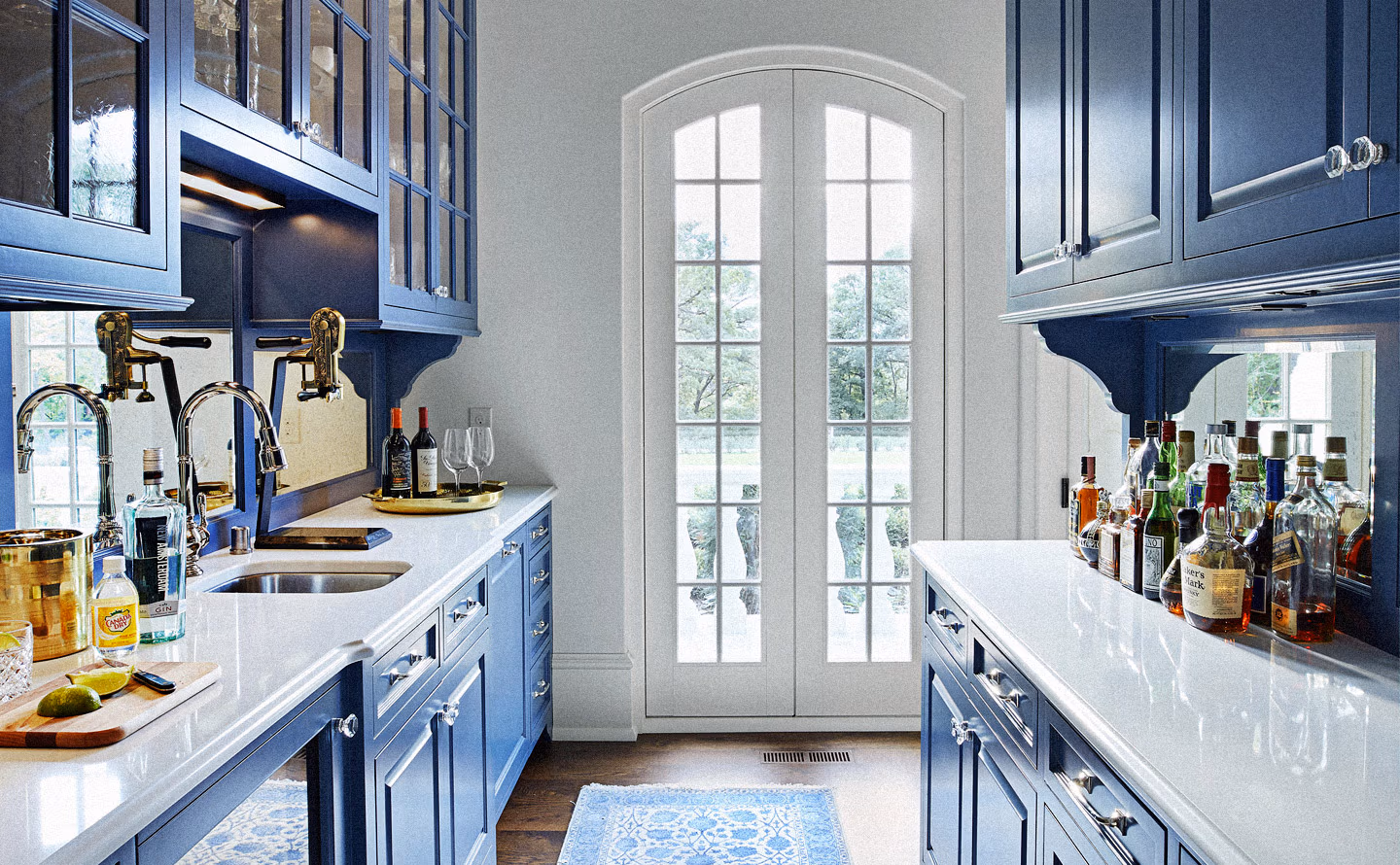 Cuisine bleu ardoise profond avec meubles shaker vitrés, plans de travail en marbre blanc veiné gris, robinetterie laiton doré vintage à leviers noirs, double porte-fenêtre cintrée blanche apportant lumière naturelle, collection de spiritueux visible, illustrant qu'un choix de couleur saturée audacieuse associé à des matériaux lumineux transforme les contraintes architecturales en opportunité décorative dramatique. Cuisine bleu ardoise profond avec meubles shaker vitrés, plans de travail en marbre blanc veiné gris, robinetterie laiton doré vintage à leviers noirs, double porte-fenêtre cintrée blanche apportant lumière naturelle, collection de spiritueux visible, illustrant qu'un choix de couleur saturée audacieuse associé à des matériaux lumineux transforme les contraintes architecturales en opportunité décorative dramatique.