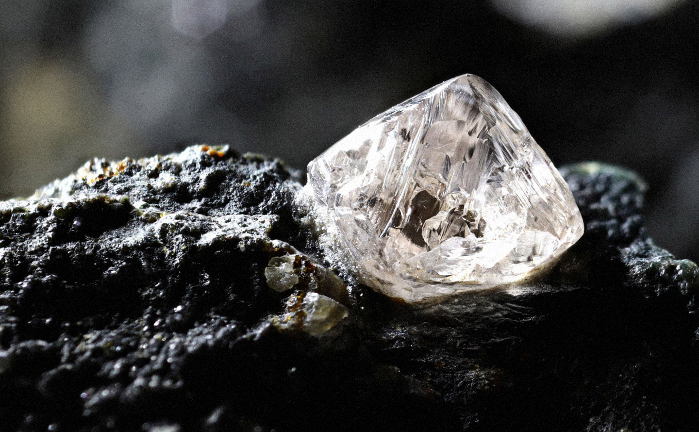 Diamant brut naturel octaédrique sur sa roche mère de kimberlite noire, montrant les inclusions cristallines caractéristiques avant la taille