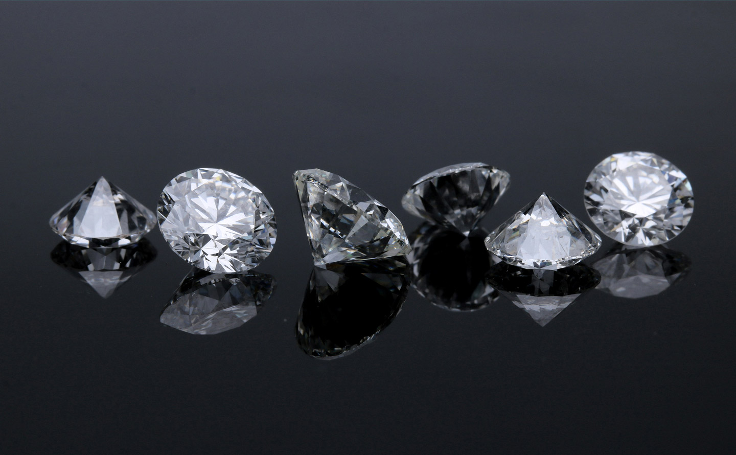 Collection de diamants taillés en rond brillant de différentes couleurs disposés sur fond noir, illustrant la diversité des pierres naturelles et synthétiques
