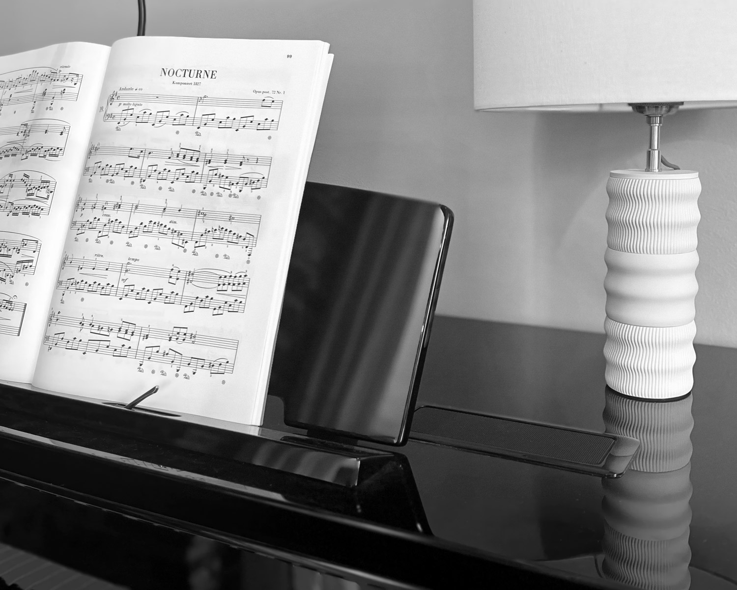 Lampe Maison Demaille Illari en configuration Onde posée sur un piano à queue noir laqué aux côtés d'une partition de Nocturne de Chopin ouverte sur pupitre, photographie en noir et blanc soulignant le dialogue entre l'objet design et l'instrument, avec reflet de la lampe dans le couvercle poli du piano Lampe Maison Demaille Illari en configuration Onde posée sur un piano à queue noir laqué aux côtés d'une partition de Nocturne de Chopin ouverte sur pupitre, photographie en noir et blanc soulignant le dialogue entre l'objet design et l'instrument, avec reflet de la lampe dans le couvercle poli du piano