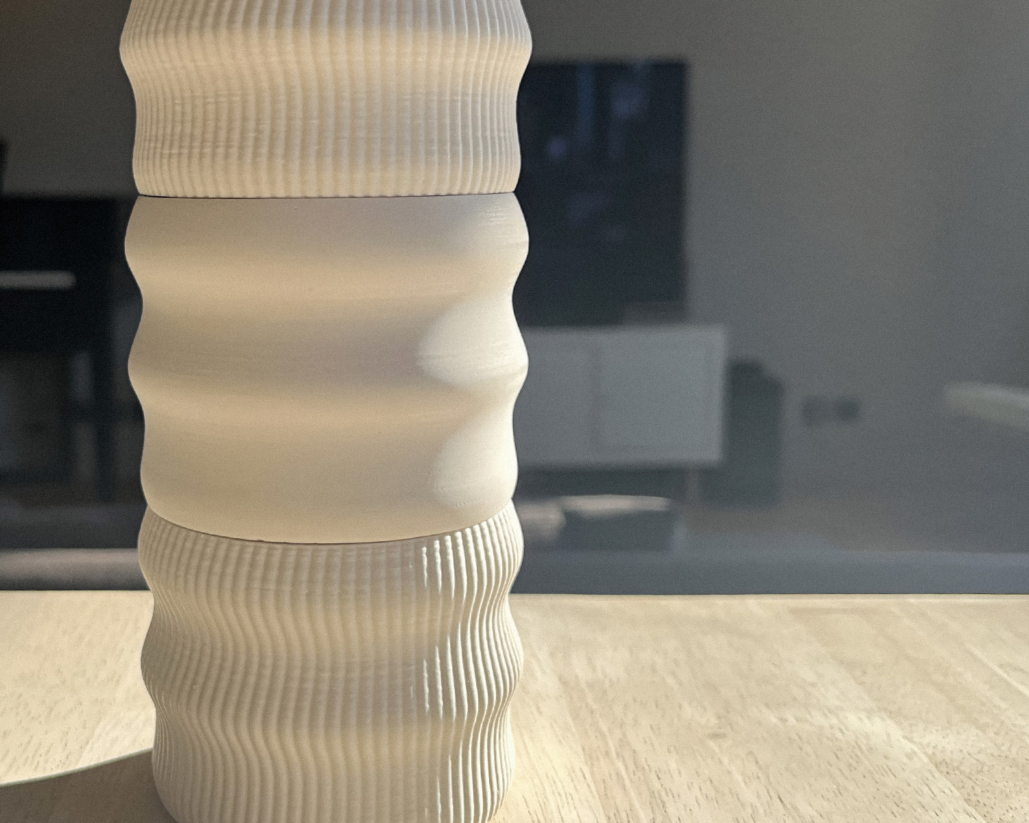 Gros plan sculptural sur socle Illari Maison Demaille en configuration Onde quadruple, stries sinueuses en blanc crème photographiées en lumière latérale rasante qui creuse chaque ondulation, posé sur surface en chêne clair avec intérieur contemporain flou en arrière-plan Gros plan sculptural sur socle Illari Maison Demaille en configuration Onde quadruple, stries sinueuses en blanc crème photographiées en lumière latérale rasante qui creuse chaque ondulation, posé sur surface en chêne clair avec intérieur contemporain flou en arrière-plan