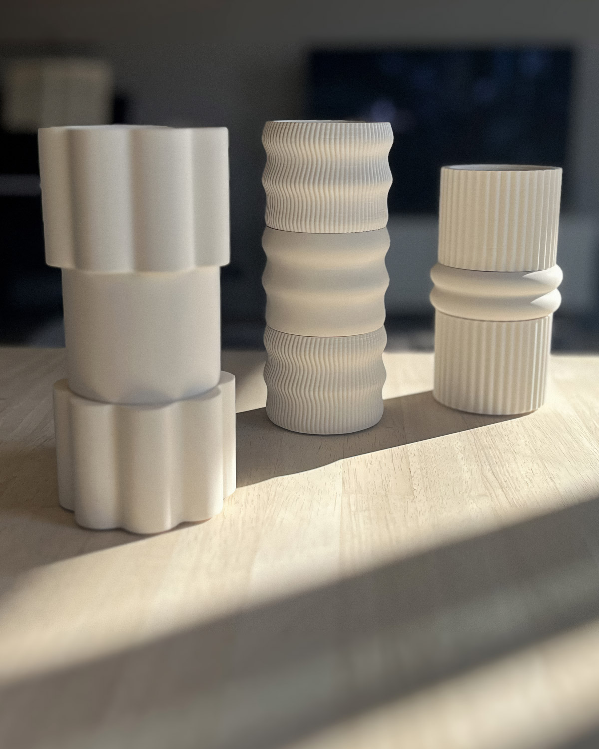 Trois compositions de socles modulables Illari Maison Demaille posées sur chêne clair dans une lumière rasante dorée : de gauche à droite, empilement Fleur et Aube aux formes organiques, colonne triple Onde aux stries sinueuses, assemblage Résonance et Anneaux aux géométries contrastées, illustrant l'étendue des silhouettes possibles en blanc mat Trois compositions de socles modulables Illari Maison Demaille posées sur chêne clair dans une lumière rasante dorée : de gauche à droite, empilement Fleur et Aube aux formes organiques, colonne triple Onde aux stries sinueuses, assemblage Résonance et Anneaux aux géométries contrastées, illustrant l'étendue des silhouettes possibles en blanc mat