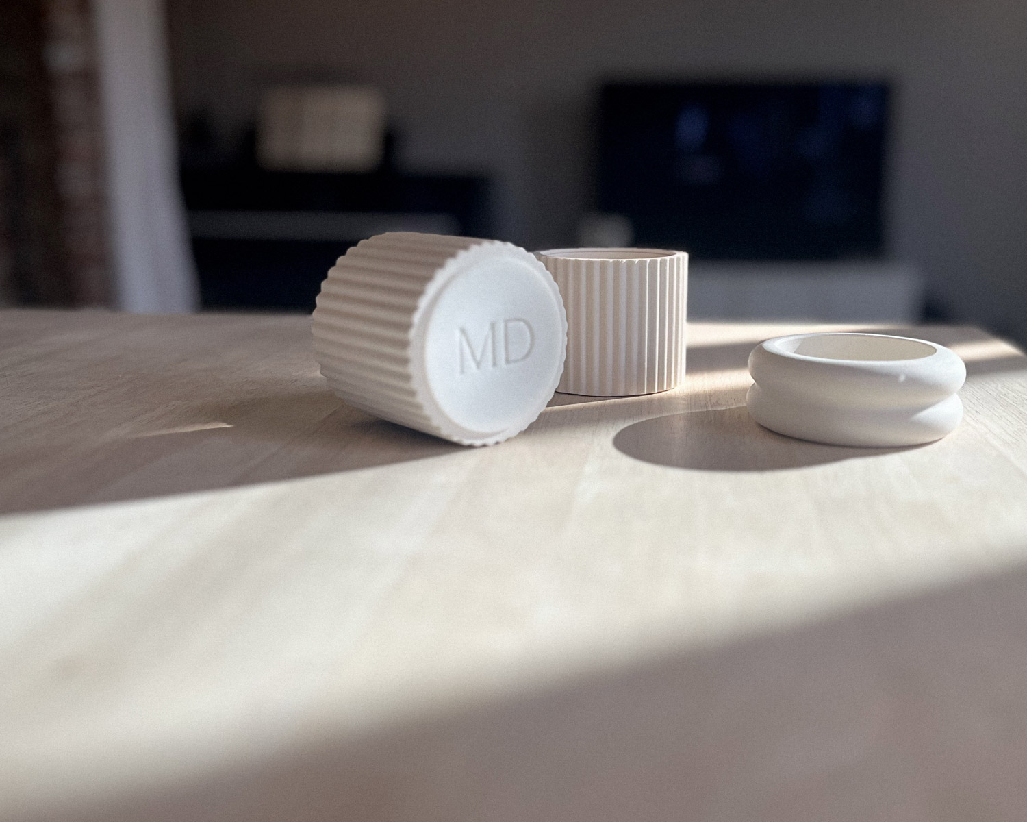Gros plan de trois modules Illari Maison Demaille posés sur surface en chêne clair : deux modules Résonance à cannelures verticales serrées dont l'un couché révèle le monogramme MD gravé en creux, accompagnés du module Anneaux à profil arrondi, dans une lumière naturelle rasante qui sculpte chaque texture Gros plan de trois modules Illari Maison Demaille posés sur surface en chêne clair : deux modules Résonance à cannelures verticales serrées dont l'un couché révèle le monogramme MD gravé en creux, accompagnés du module Anneaux à profil arrondi, dans une lumière naturelle rasante qui sculpte chaque texture